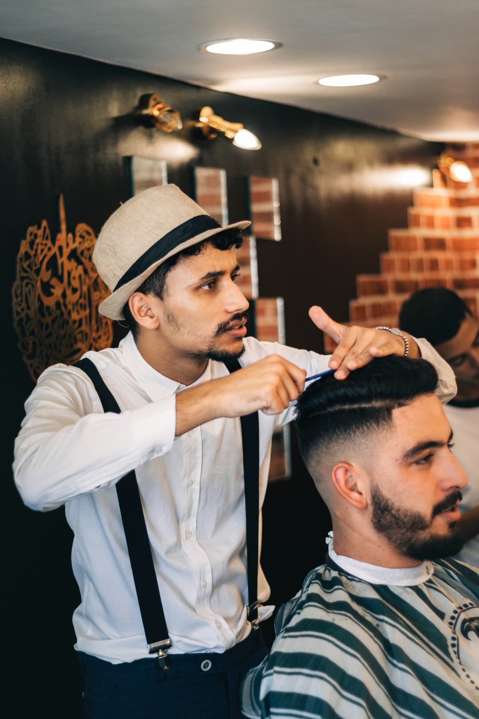 A barber in a hat styling a client's hair.