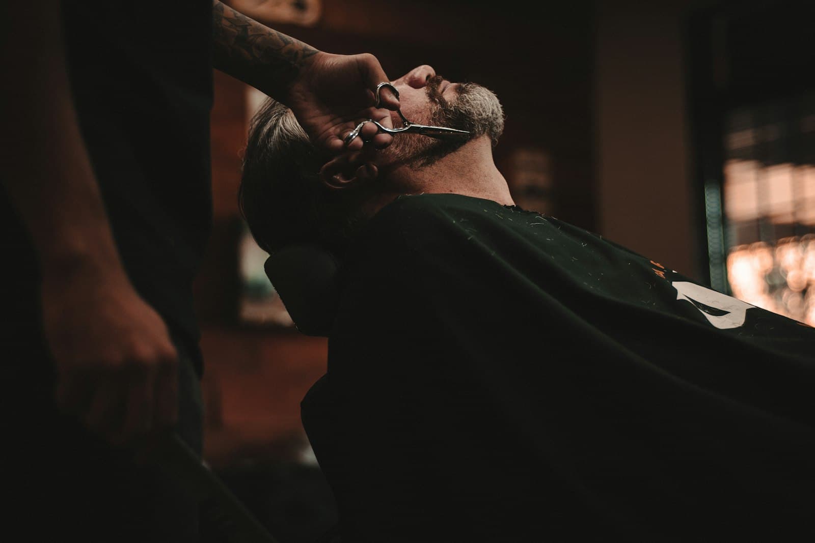 A barber trimming a client's beard with shears.